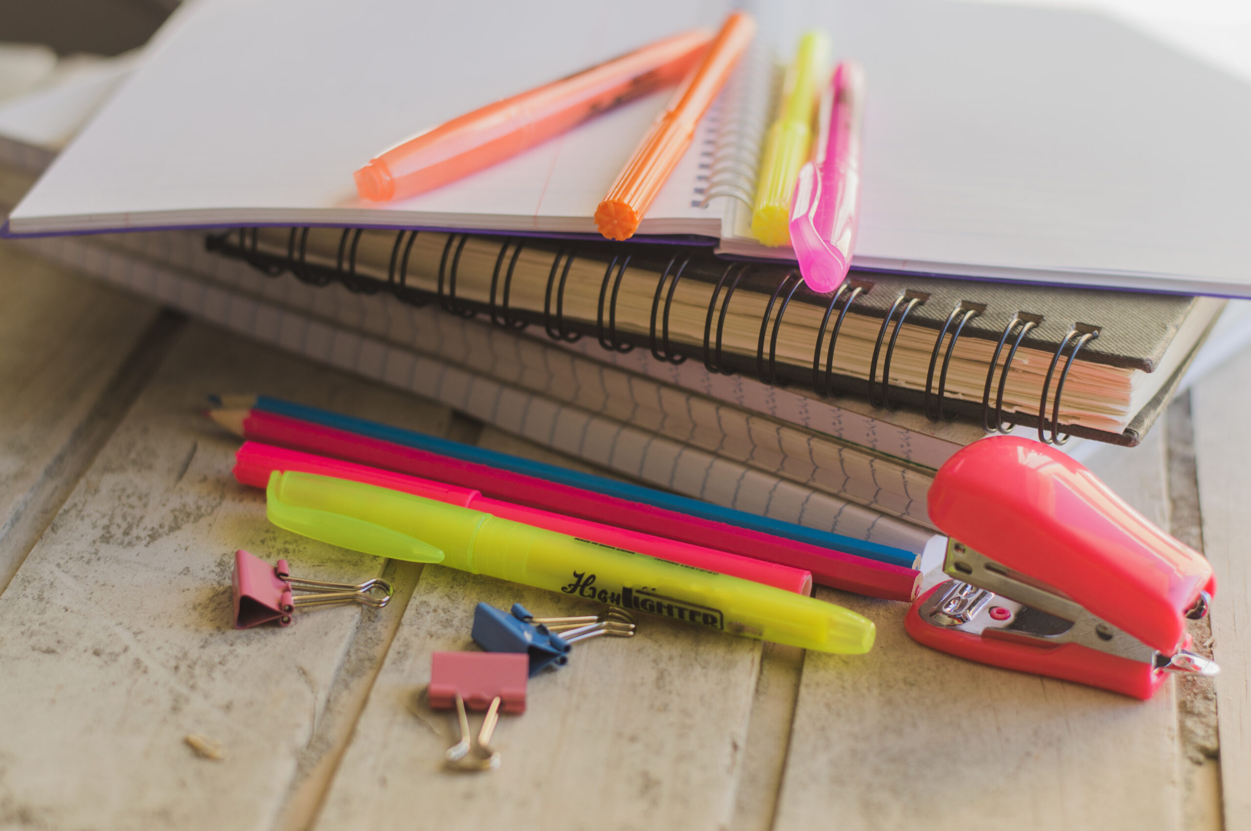 tas de cahiers avec des stylos et un agrafeuse rose