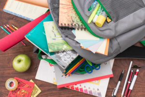 un sac d'écolier se vide avec une pomme, un rouleau de scotch, des stylos et carnets